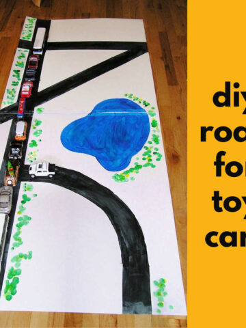 Diy road for toy cars made from large matte board. Toy vehicles sit on the black road.