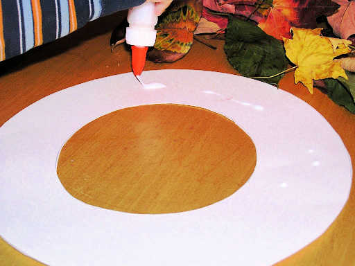 Squeezing school glue on white wreath shaped paper circle