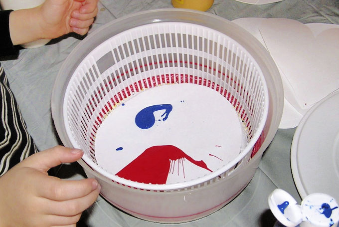 Salad spinner with paper and blobs of red and blue paint inside