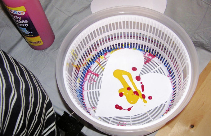 Salad spinner with heart shaped paper inside with yellow and red blobs of paint