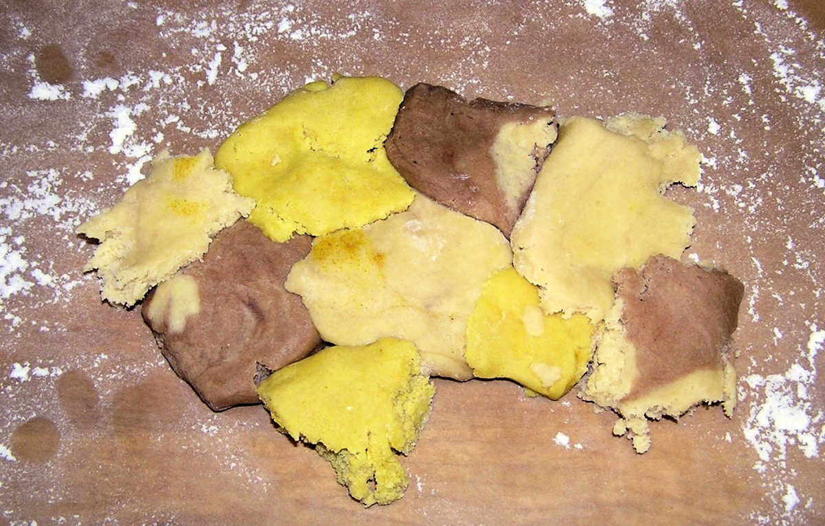 Ball of cookie dough using yellow, brown and natural colored dough on floured cutting board