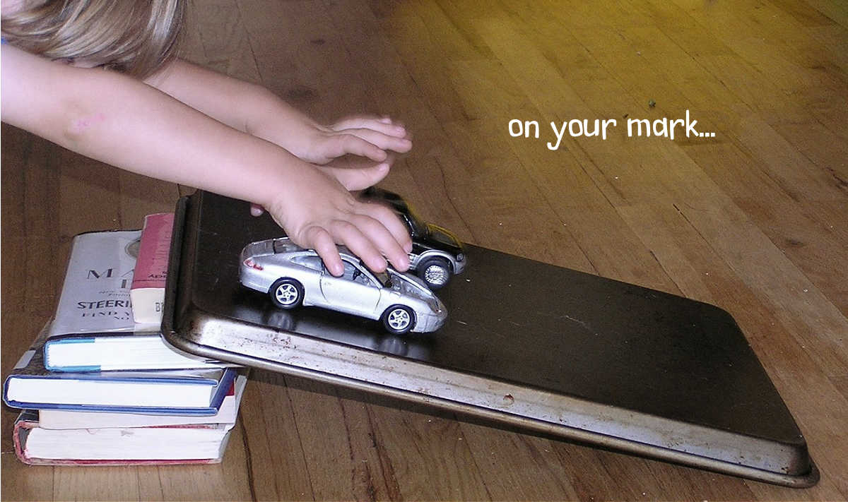 Child rolling two toy cars down homemade ramp for toy vehicles