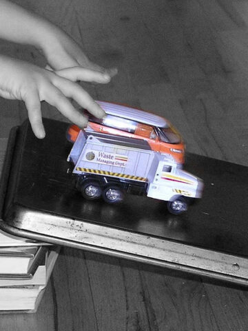 Child rolling toy truck and toy bus down diy ramp for toy cars made from baking sheet and book stack
