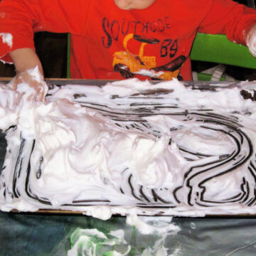 Child in orange shirt with hands in shaving cream on sensory tray