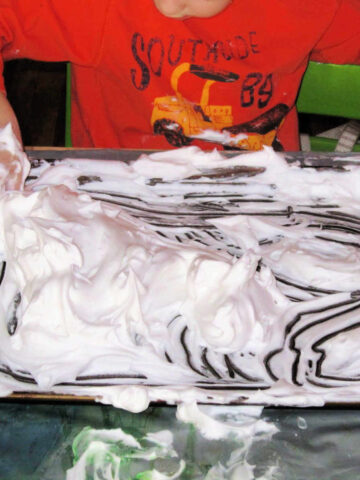 Child in orange shirt with hands in shaving cream on sensory tray