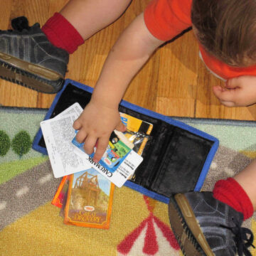 toddler playing with cards in toy wallet on floor