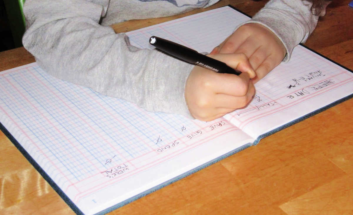 Child writing in accounting ledger.
