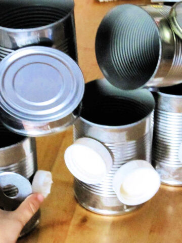 Child's hand reaching for empty tin cans and plastic caps as part of magnet building set