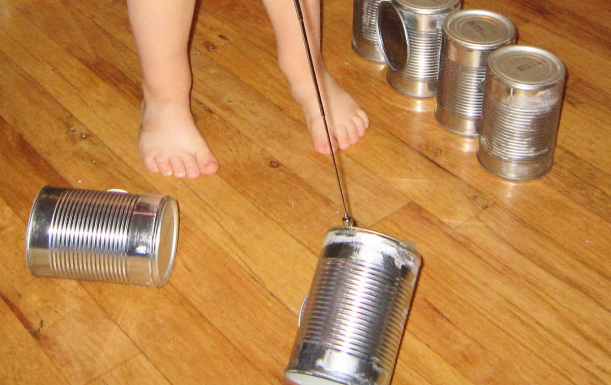 Child picking up empty tin can with telescoping pick up tool. More tin cans on the flor next to feet.