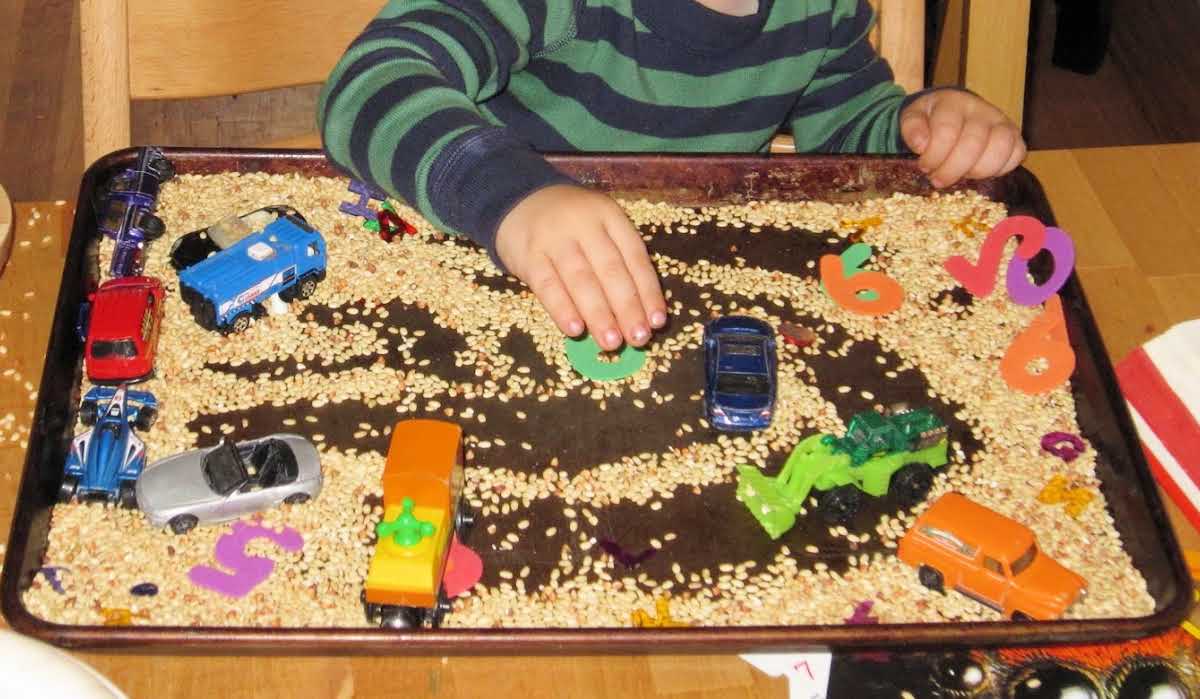 Child playing with cars in tray of rice