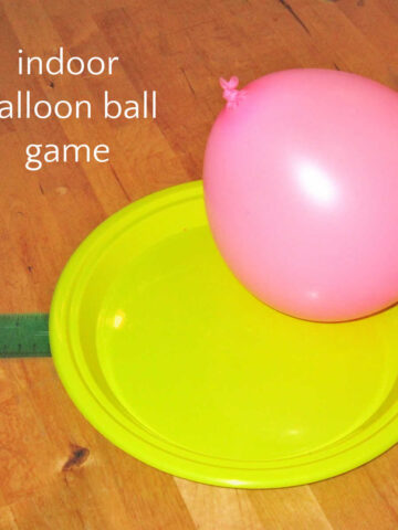 Pink balloon resting on paddle made from plastic plate for indoor balloon ball game