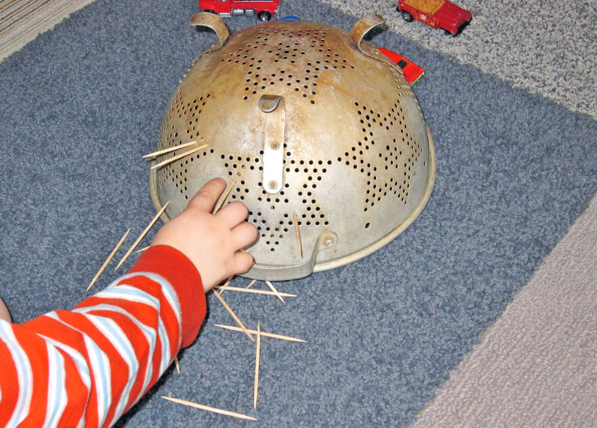 Child pressing toothpicks through holes in a colander