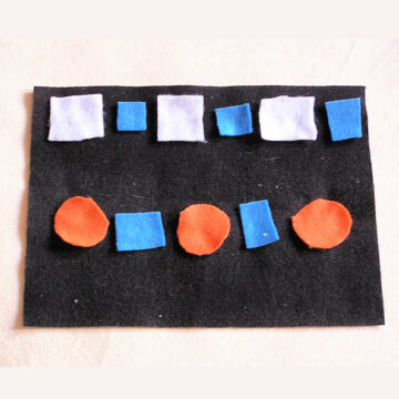 White and blue square and orange circle felt shapes on black background laid out in white square-blue square and orange circle-blue square pattern.
