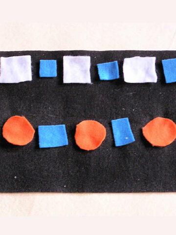 White and blue square and orange circle felt shapes on black background laid out in white square-blue square and orange circle-blue square pattern.