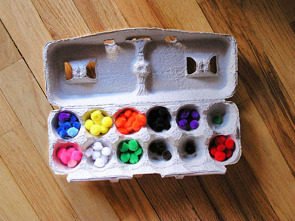 Pom poms sorted by color in an egg carton