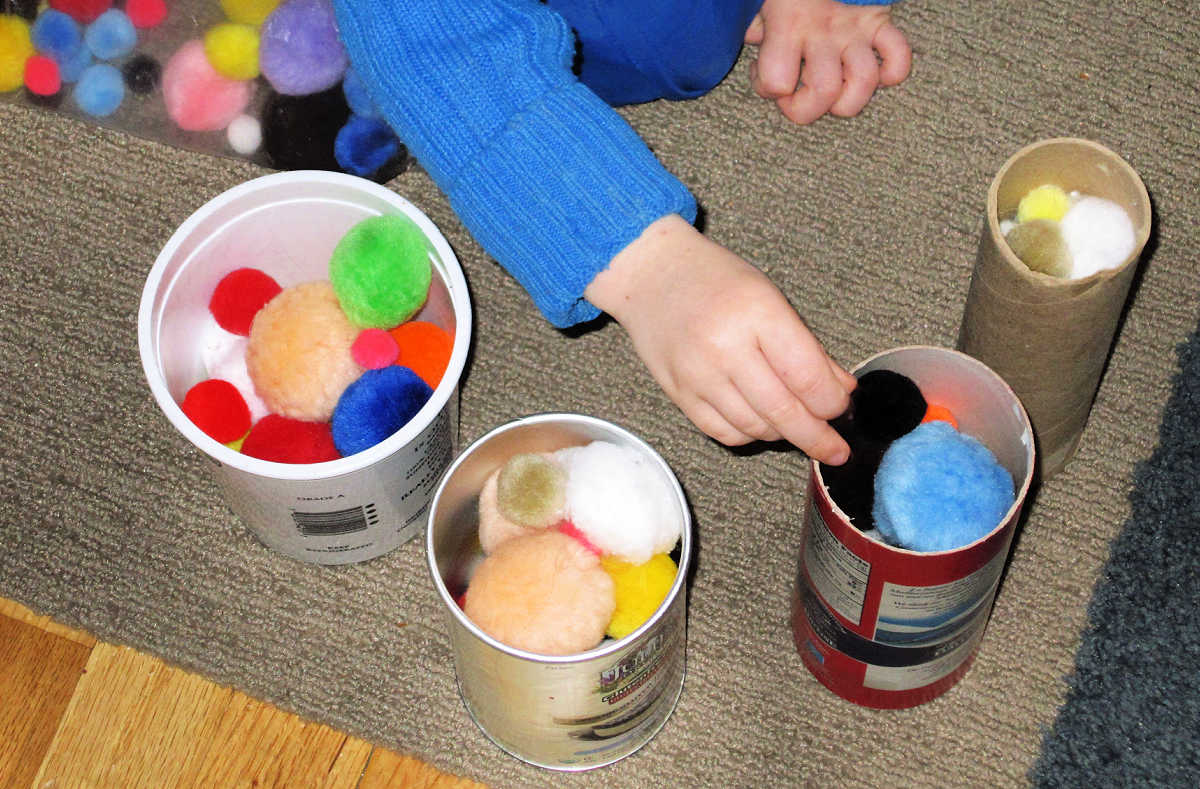 Child sorting pom poms into containers