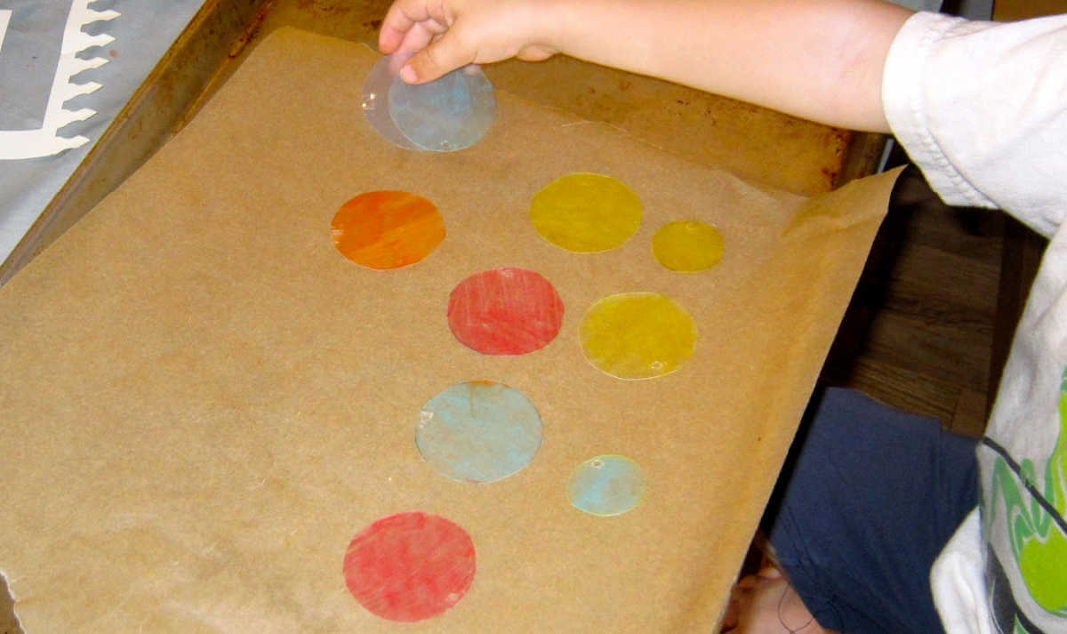 Child placing circles of shrink plastic on baking tray