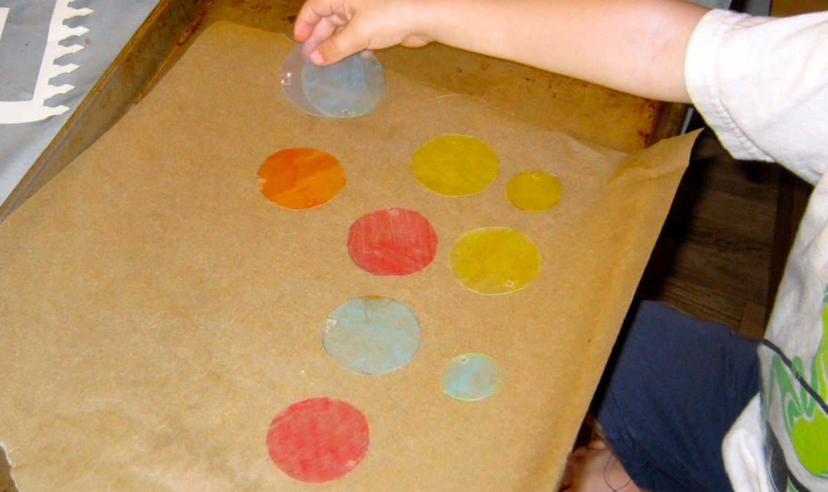 Child placing circles of shrink plastic on baking tray