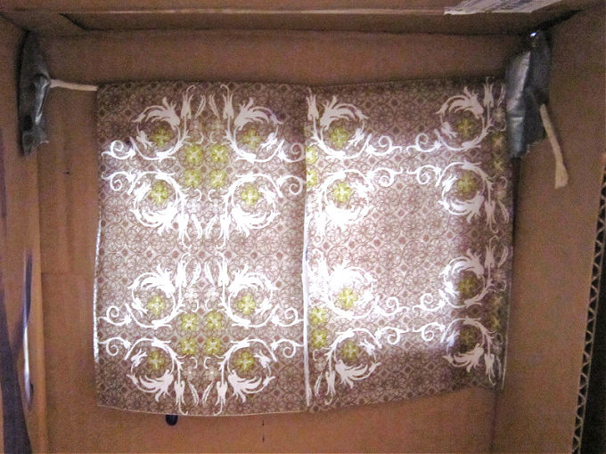 Inside cardboard box showing napkin curtains on string taped to box