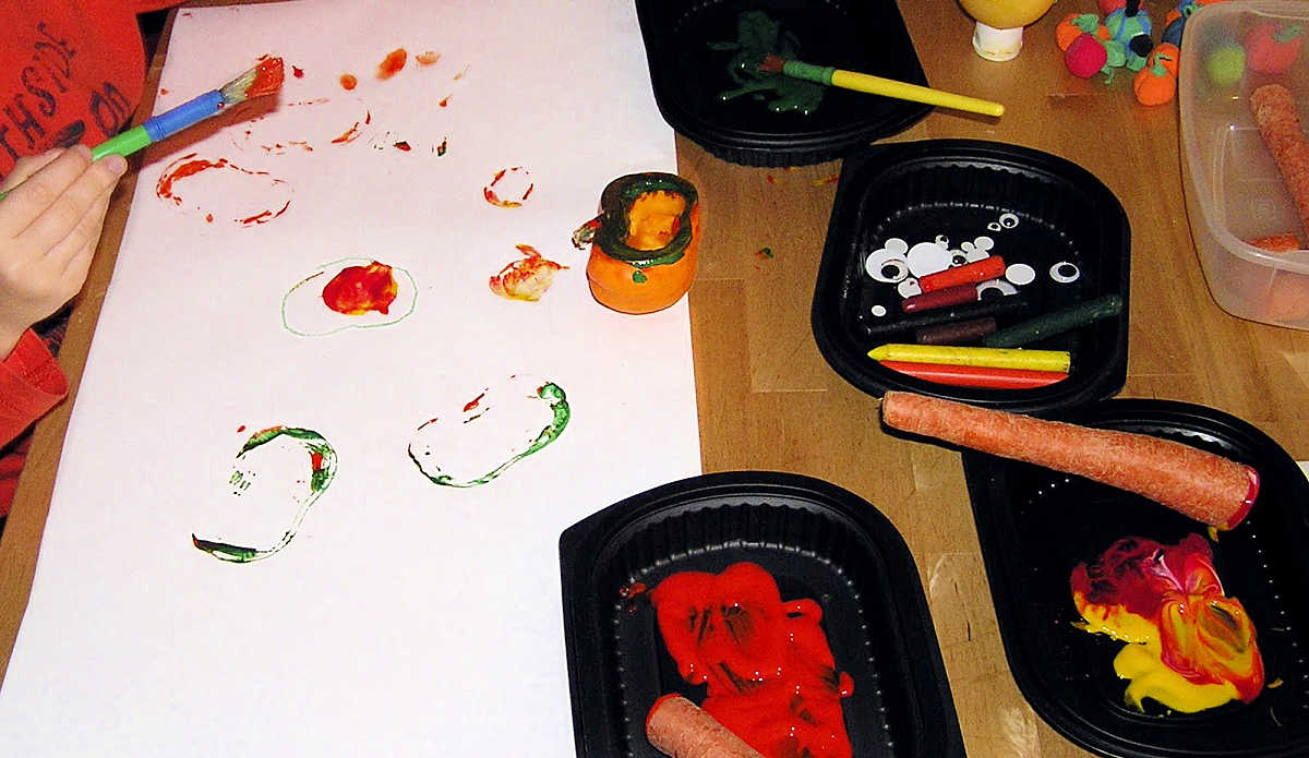 Child painting with pumpkin half and root vegetables
