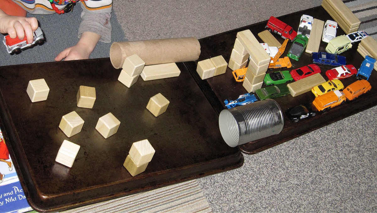 Toy blocks and cars on a diy obstacle course made from baking sheets