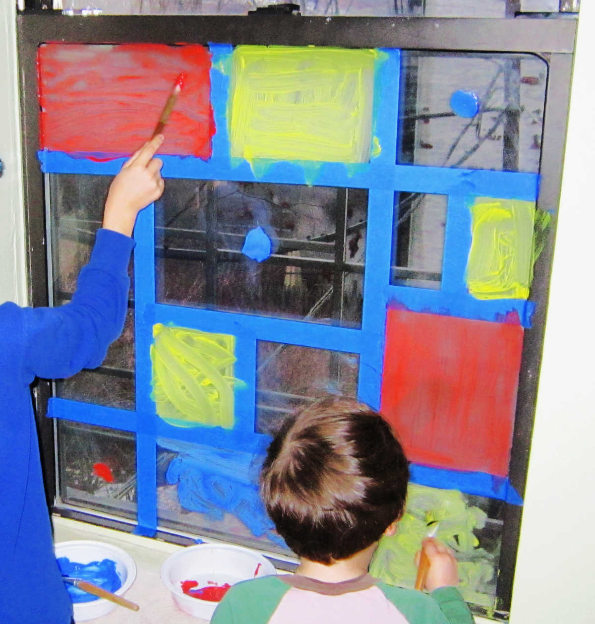 Kids painting on window covered in blue tape.