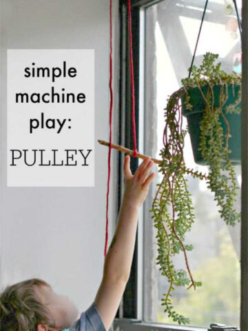 Child reaching for stick hanging from a pulley in front of a window.