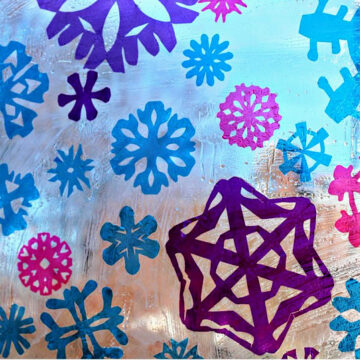Cellophane snowflakes in blue, pink and purple stuck to window glass, creating a stained glass effect.