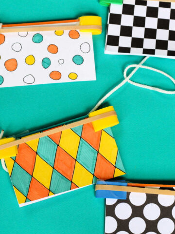 Three noise makers made from decorated index cards, rubber bands stretched across the top and string.