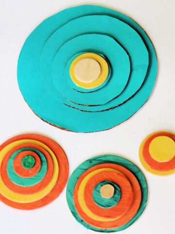 Four piles of concentric circles made from blue, orange and yellow cardboard for tower of Hanoi puzzler game.