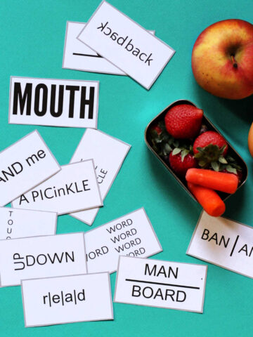 Collection of wuzzle word puzzle lunch box notes scattered next to apple, egg and small tin of snacks.
