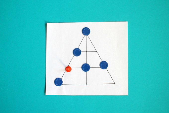 Len Choa game board in shape of triangle bisected by two lines with six blue tokens surrounding one orange token.