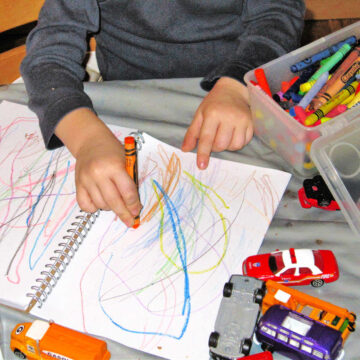 Child scribbling on preschool journal page with crayons