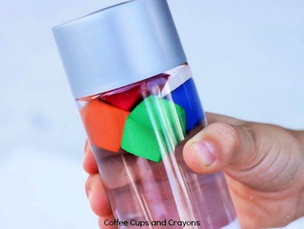 Hand holding a sink or float science experiment water bottle containing colorful blocks