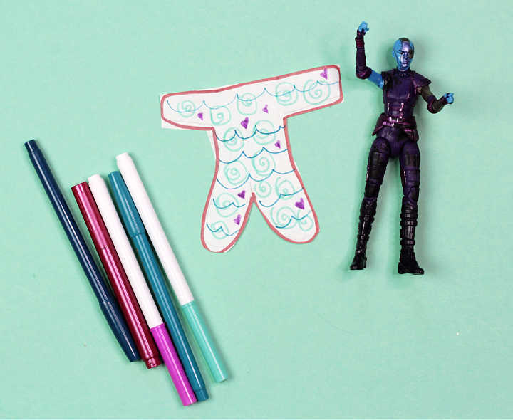 Action figure and cut out mermaid tail next to group of markers.
