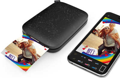 Black Sprocket printer printing photo next to mobile phone showing same photo.