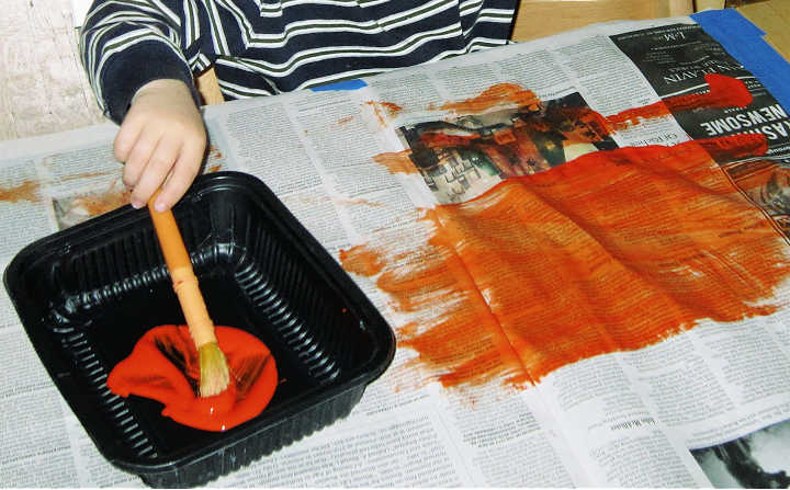 Child painting newspaper with orange paint