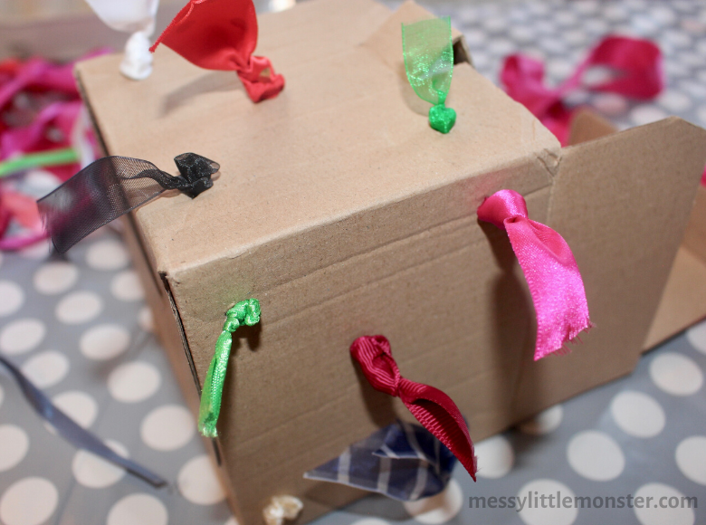 Ribbons attached to a cardboard box activity for babies