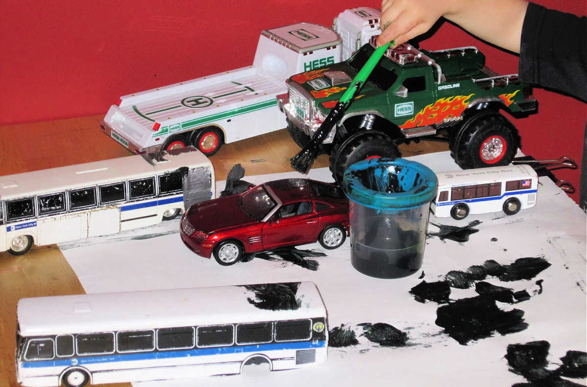 child Painting toy vehicles with black paint 