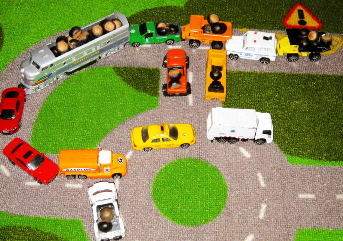 Toy cars on road rug with toy trains and toy trucks full of acorns