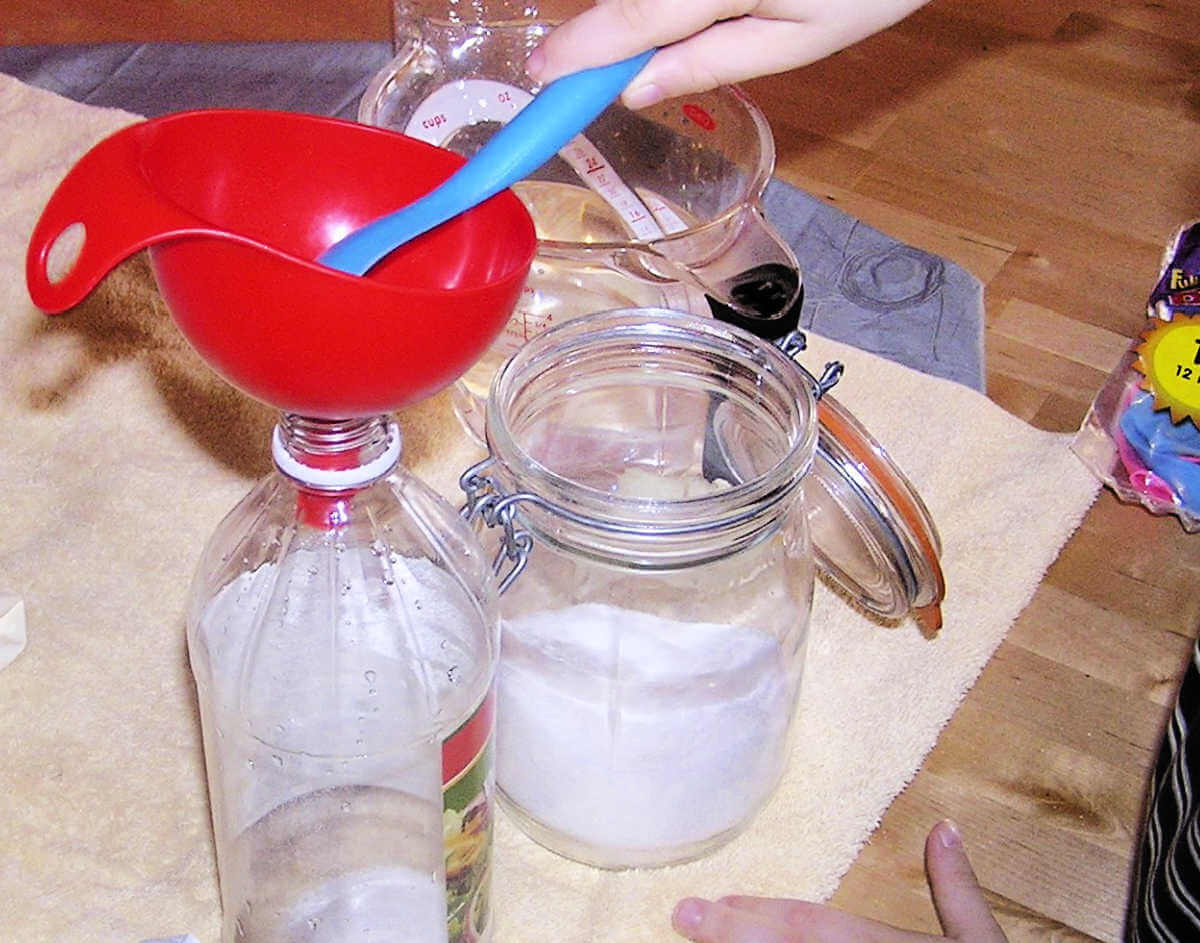 Child's hand using blue spoon to but sugar from glass storage jar into empty plastic bottle