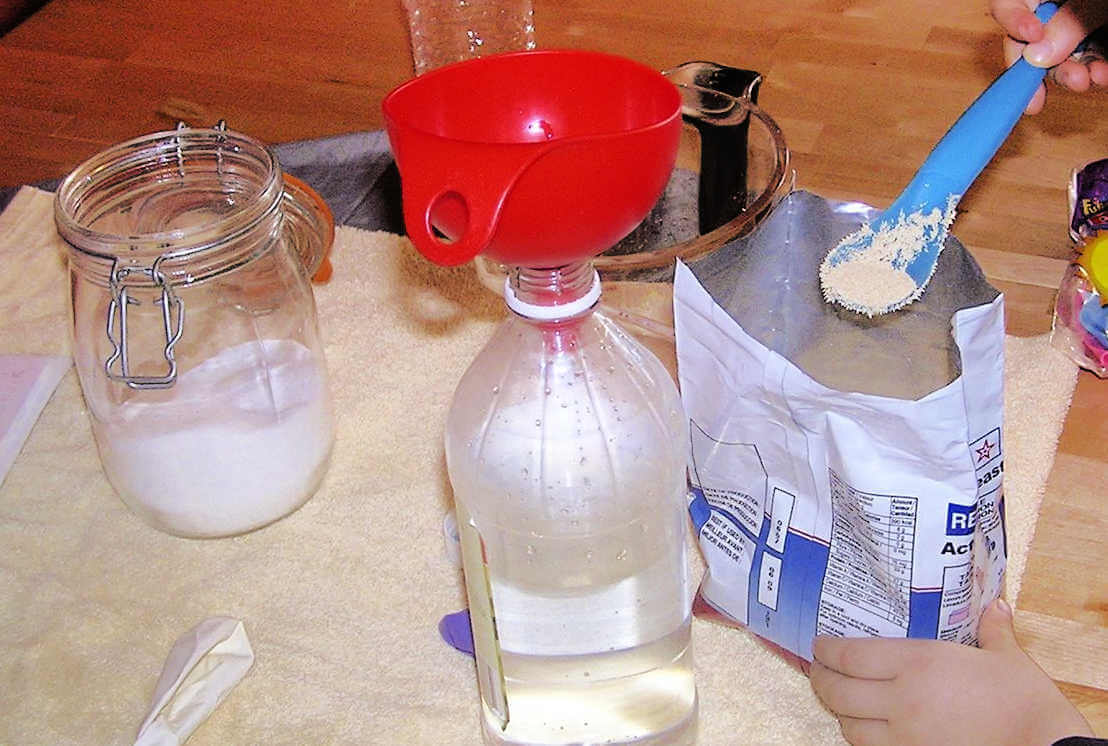 Child spooning yeast into funnel resting in bottle filled with water