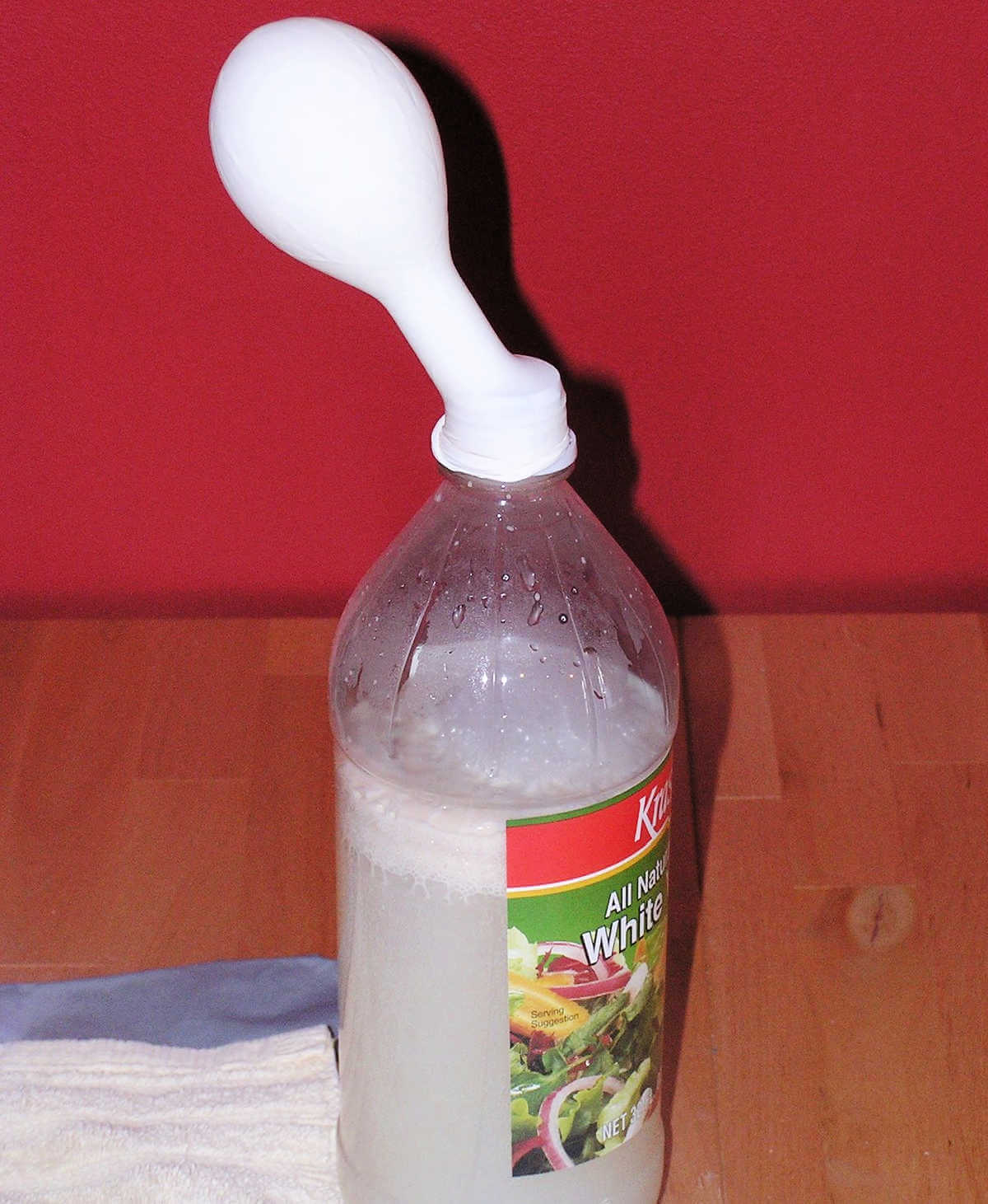 Small white balloon on next of bottle standing upright and slightly inflated.