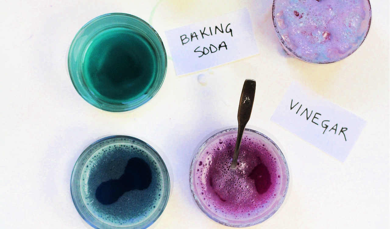 Glass jars of purple and green liquid with labels for baking soda and vinegar