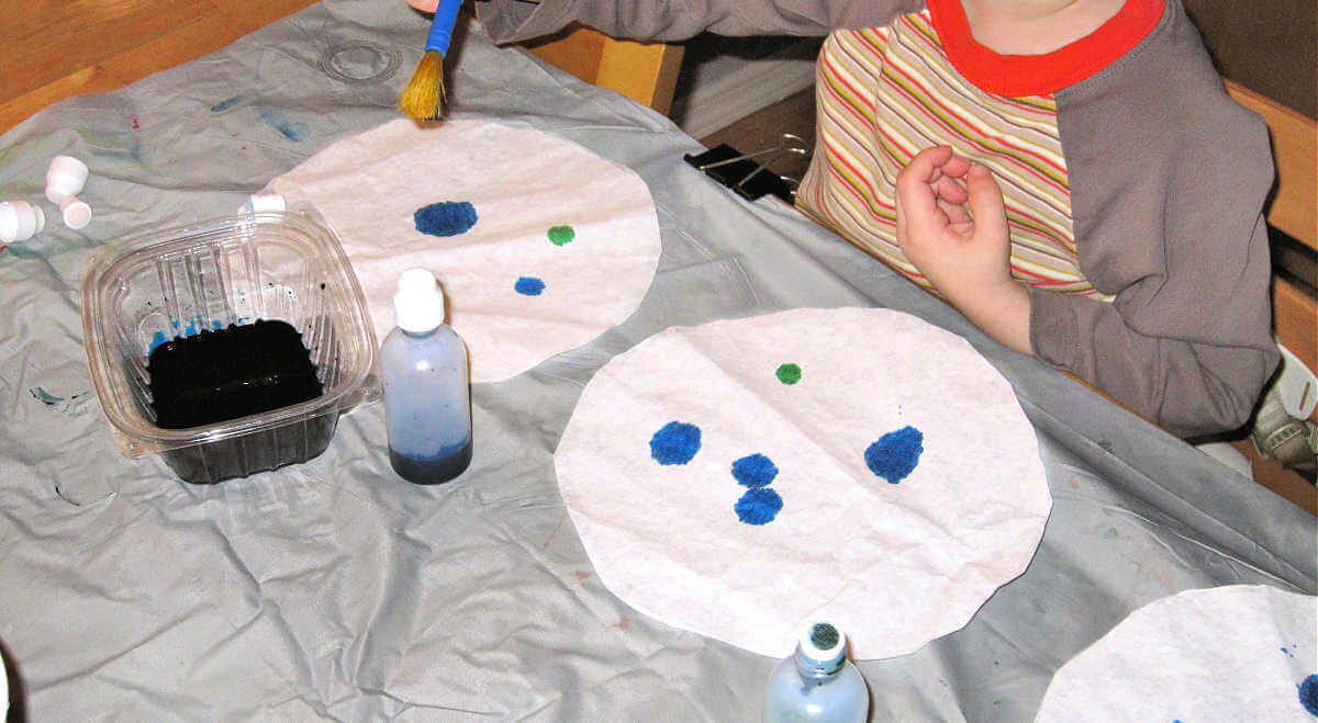 Child applying blue paint to three large coffee filters
