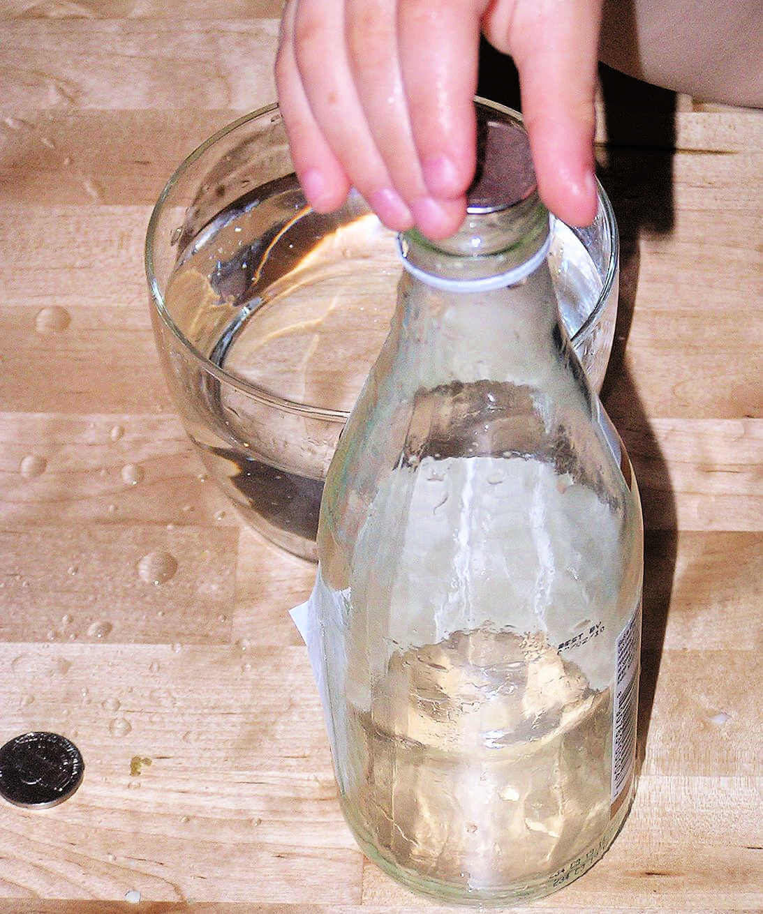Child hand placing coin on the top of a glass bottle partially filled with water
