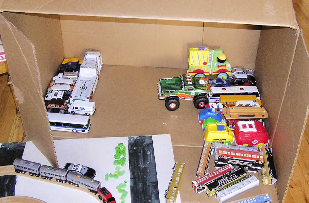 toy vehicles lined up inside large cardboard box parking garage