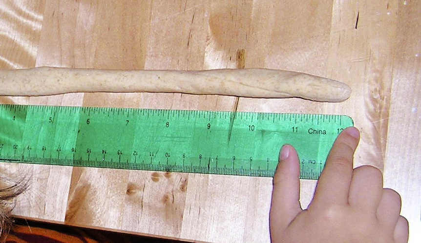green ruler on table next to long stretch of pretzel dough