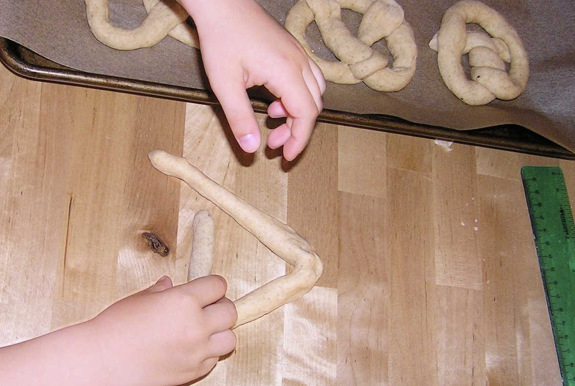 Child hands shaping pretzel dough into the letter A
