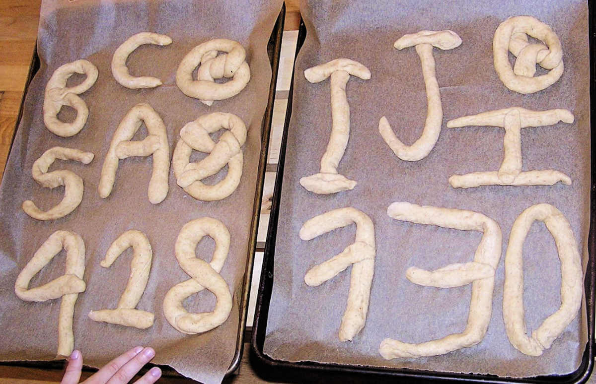 two trays of unbaked pretzel number and letter shapes
